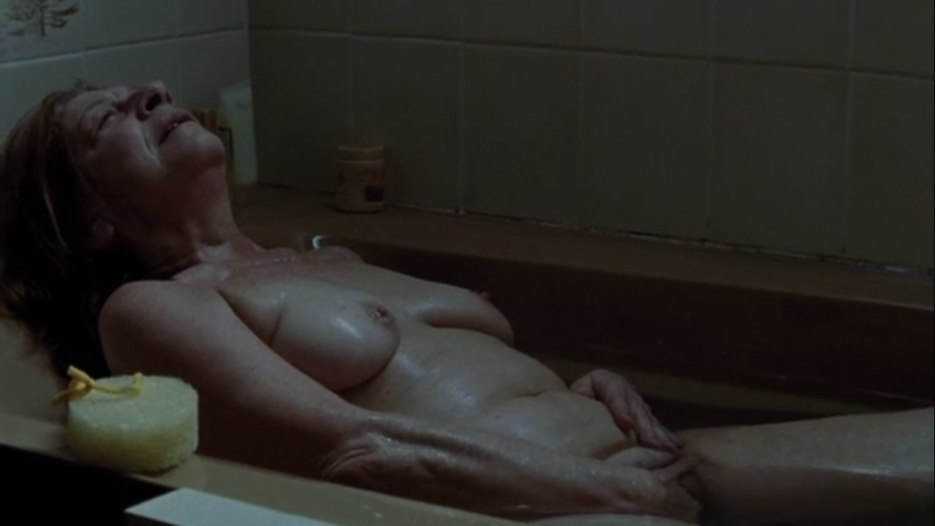 Cena do filme Irene. Mulher velha deitada na banheira. Ela está nua, com o corpo molhado, de barriga para cima, se masturbando com a mão direita entre as pernas.
