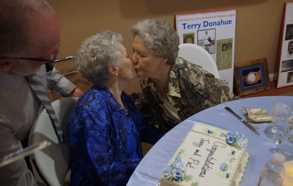 Cena do filme Secreto e proibido. Terry e Pat se beijam. Elas são velhas, de cabelo branco curto, e estão sentadas a uma mesa com um bolo e copos, na festa de casamento.