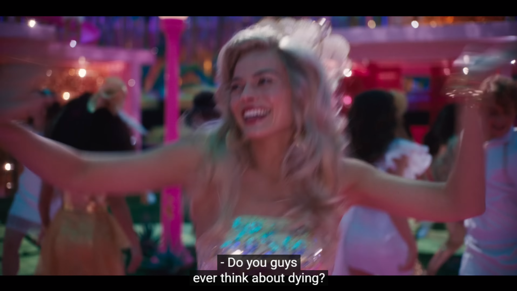 Cena de Barbie. A jovem Margot Robbie dança sorrindo e pergunta: "Alguma vez vocês já pensaram na morte?".